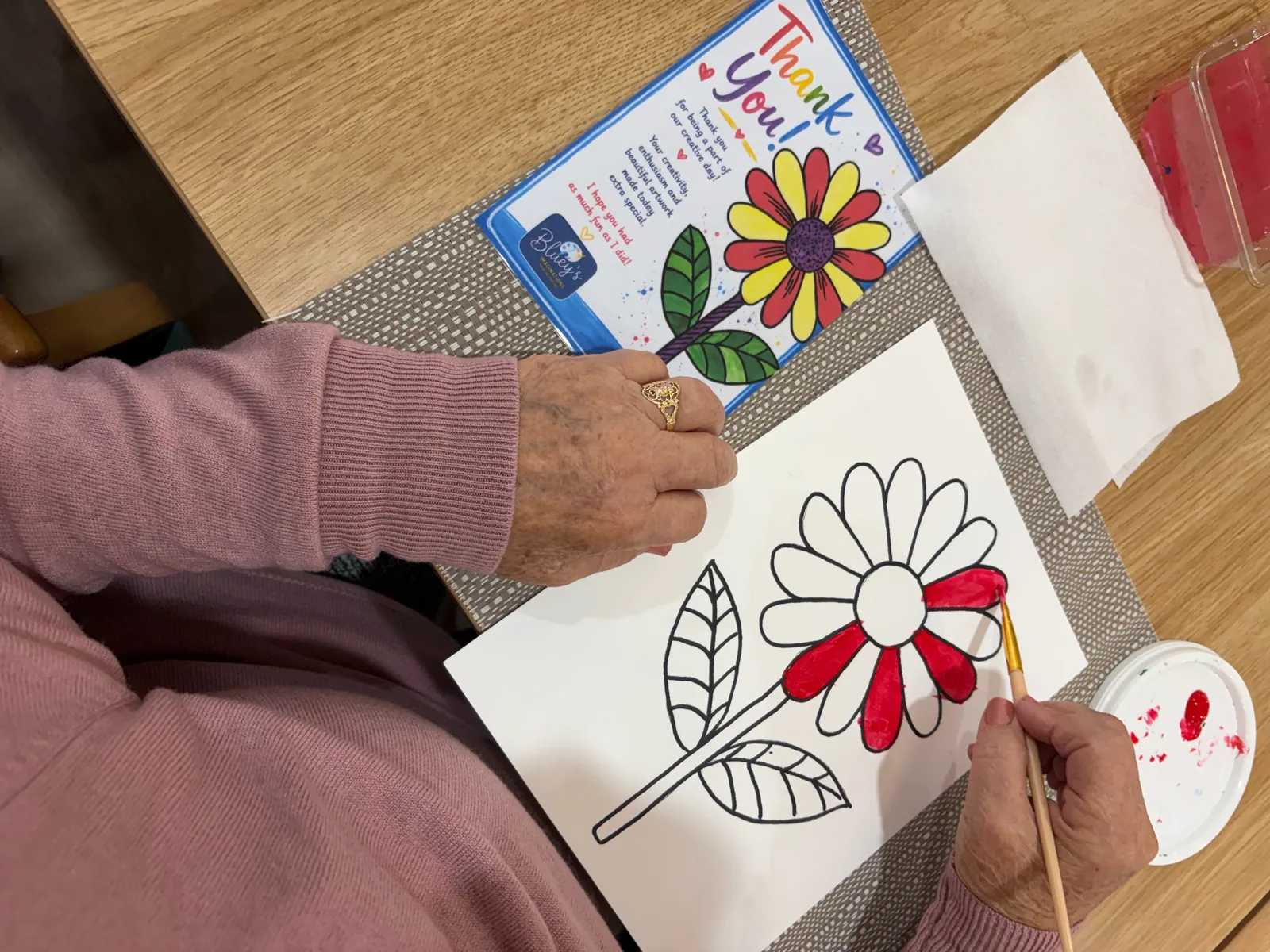 A participant painting a bright flower canvas at an aged care art workshop