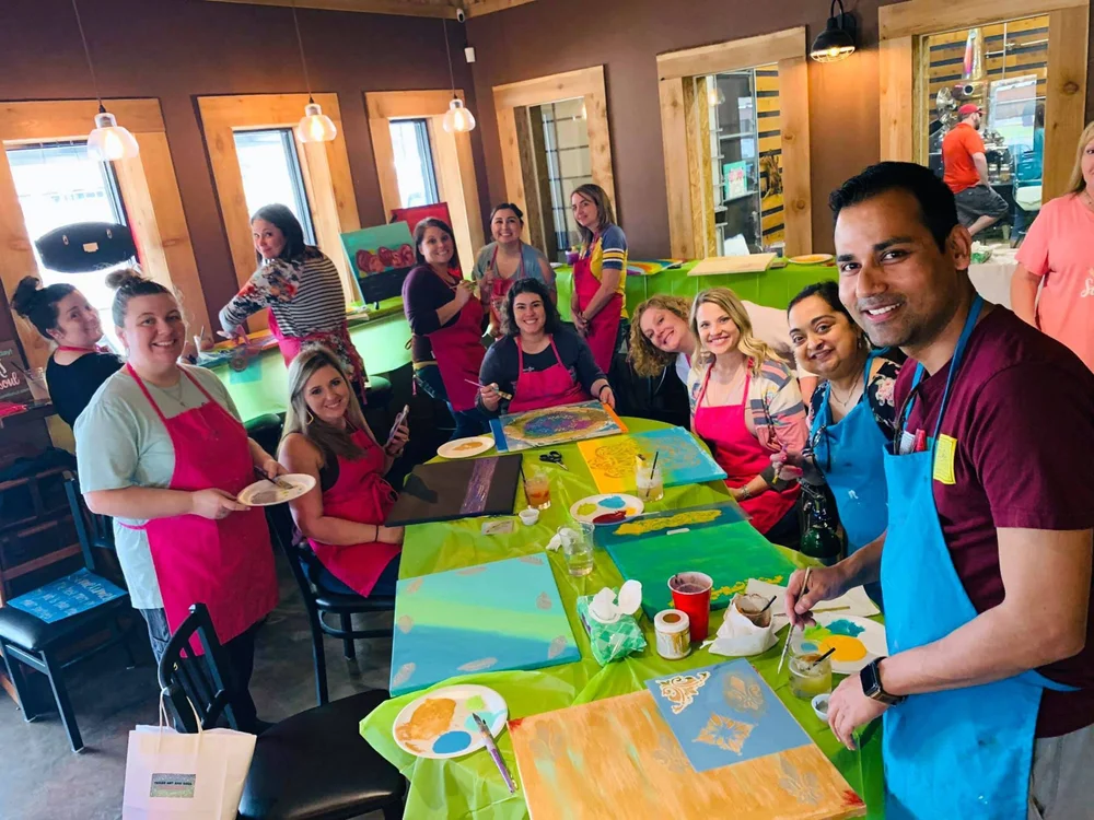 A large group of friends gathered around painting tables in the studio